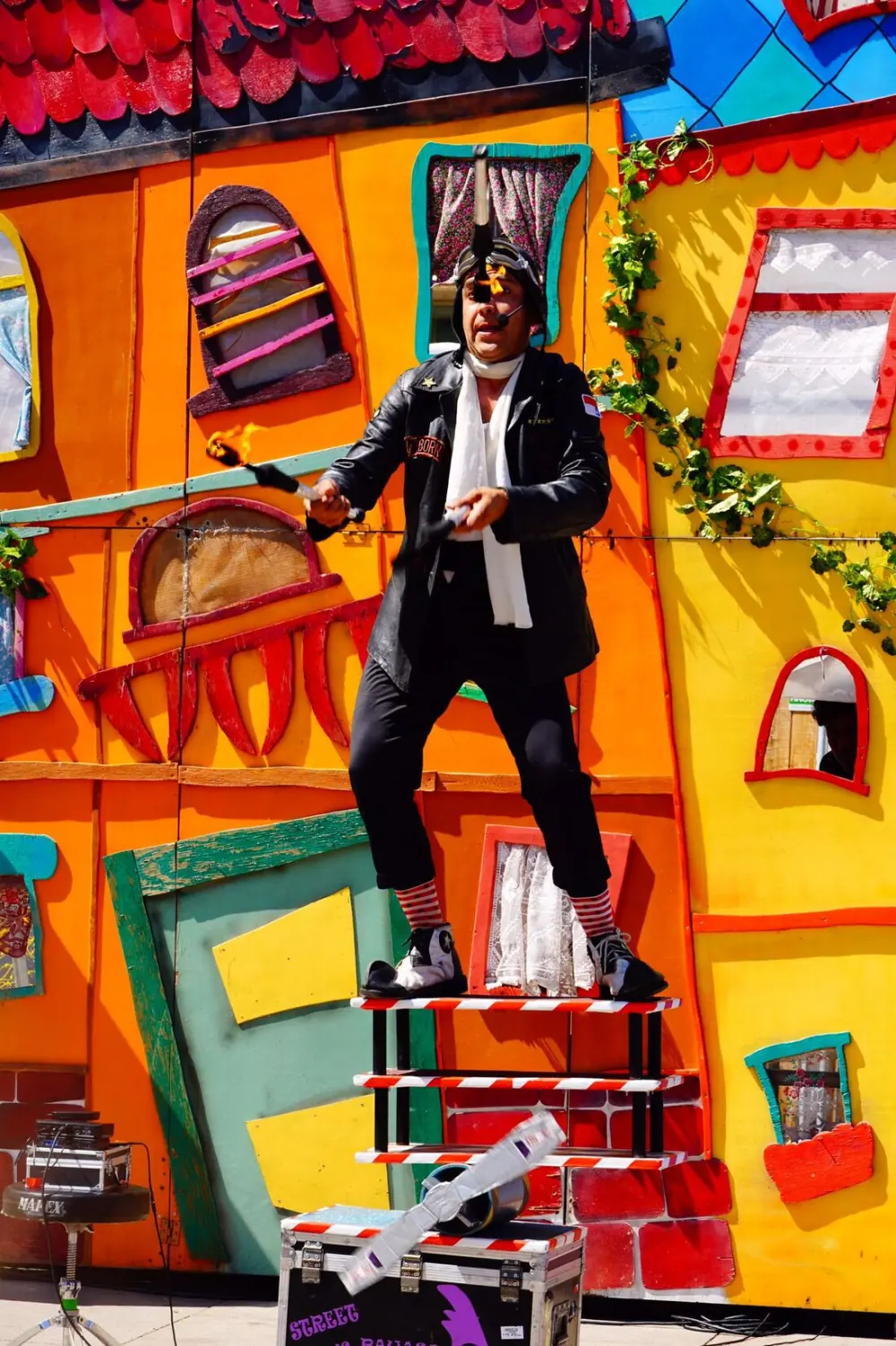 Payaso Solutto en equilibrio sobre una torre de sillas, frente a un decorado pintado